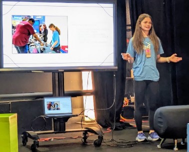 A young person stands on a stage presenting information to educators